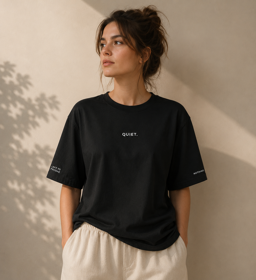 Woman wearing a black t-shirt with 'QUIET' text against a beige wall.